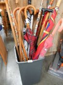 A plastic bin full of walking sticks and umbrella's.