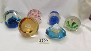 Five glass paperweights and a perspex Royal Mint paperweight inset with £1 coin.