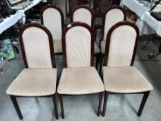 A set of six dark wood stained dining chairs with cream seats.