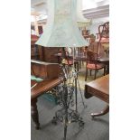 An ornate wrought iron and brass standard lamp with shade.
