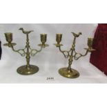 A pair of heavy brass candelabra with birds on top.