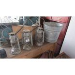 Three hurricane lamps and a galvanized bucket.