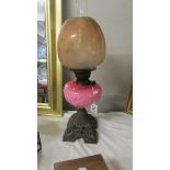 A 19th century oil lamp with pink glass font on a cast iron base and with original acid etched