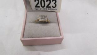 A diamond ring set with Princess cuts to centre and round brilliant cuts to edges and shoulders in