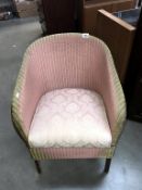 A pink Lloyd Loom chair with storage compartment