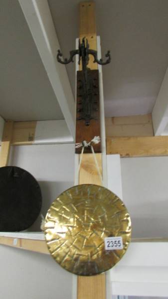 A brass dinner gong on wall mounting metal bracket.