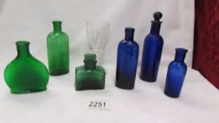 Three blue glass bottles, three green glass bottles and a measuring glass.