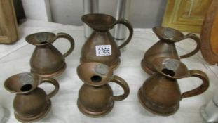 Six copper jugs in assorted sizes.
