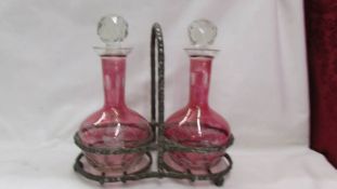 A cranberry glass oil and vinegar set of metal stand.