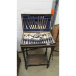 A canteen of cutlery in an oak barley twist leg stand.