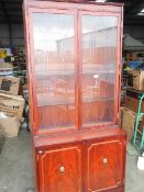 A mahogany effect inlaid display unit with bevel cut doors and storage below.