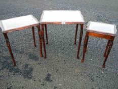 A nest of 3 tables with leather insets and glass tops.