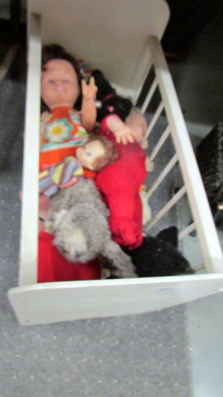 A doll's cot with dolls and soft toys.