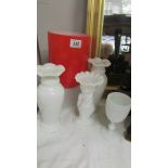 A large red vase and four white glass vases.