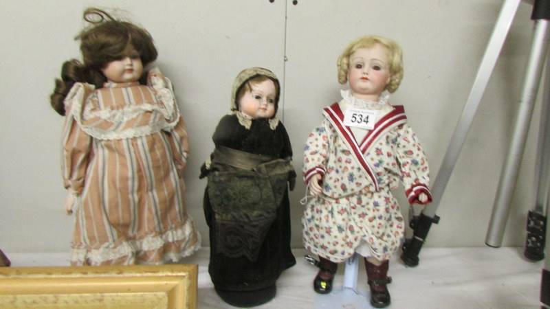 Two old porcelain dolls and another with a bottle as its body.