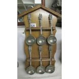 A set of six ladles with figural handles on an oak rack.