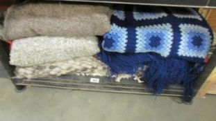 A quantity of throws and a blue crocheted blanket.