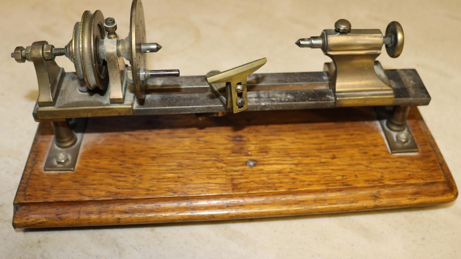 A small brass model of a basic wood turning lathe. Mounted on a hardwood plinth. Intended to be a