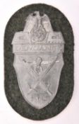 A Third Reich Demjansk Shield, of silver coloured metal on field grey patch with paper backing. Near