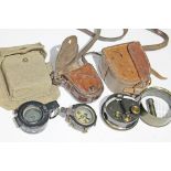 A group of three military compasses with cases.
