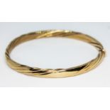 A gold bangle of twisted form, marked 9Kt and also with 9ct gold import marks, approx. diam. 6cm,
