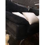 A black upholstered three seater sofa with additional white/cream cushions