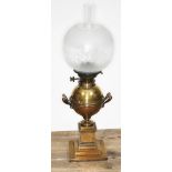 A Hinks brass oil lamp of urn form on column with weighted and stepped base, glass shade and flu,