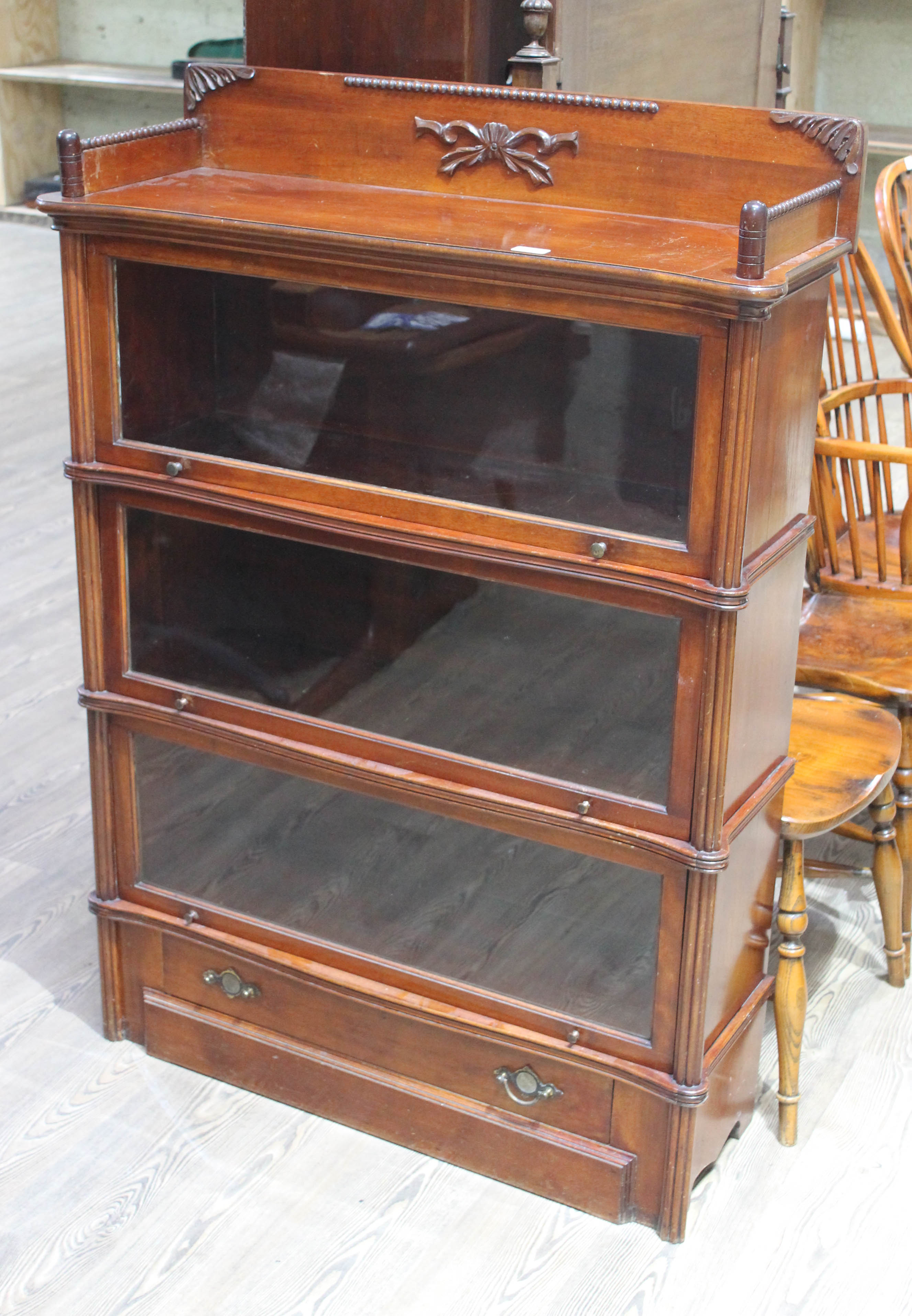 A three part mahogany sectional bookcase of shaped form with gallery, faux columns and lower drawer,