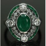 An Art Deco style diamond and emerald ring, the central oval cut and bezel set emerald weighing