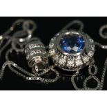 A sapphire and diamond cluster pendant on chain, the central bezel set round mixed cut sapphire