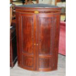 A George III bow front inlaid mahogany corner cabinet with dentilated moulding, shell inlay and