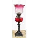 A Victorian cast iron oil lamp with ruby glass reservoir and etched cranberry glass shade, height