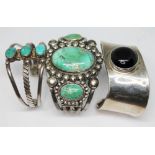 A group of three white metal bangles comprising two set with turquoise cabochons and another of