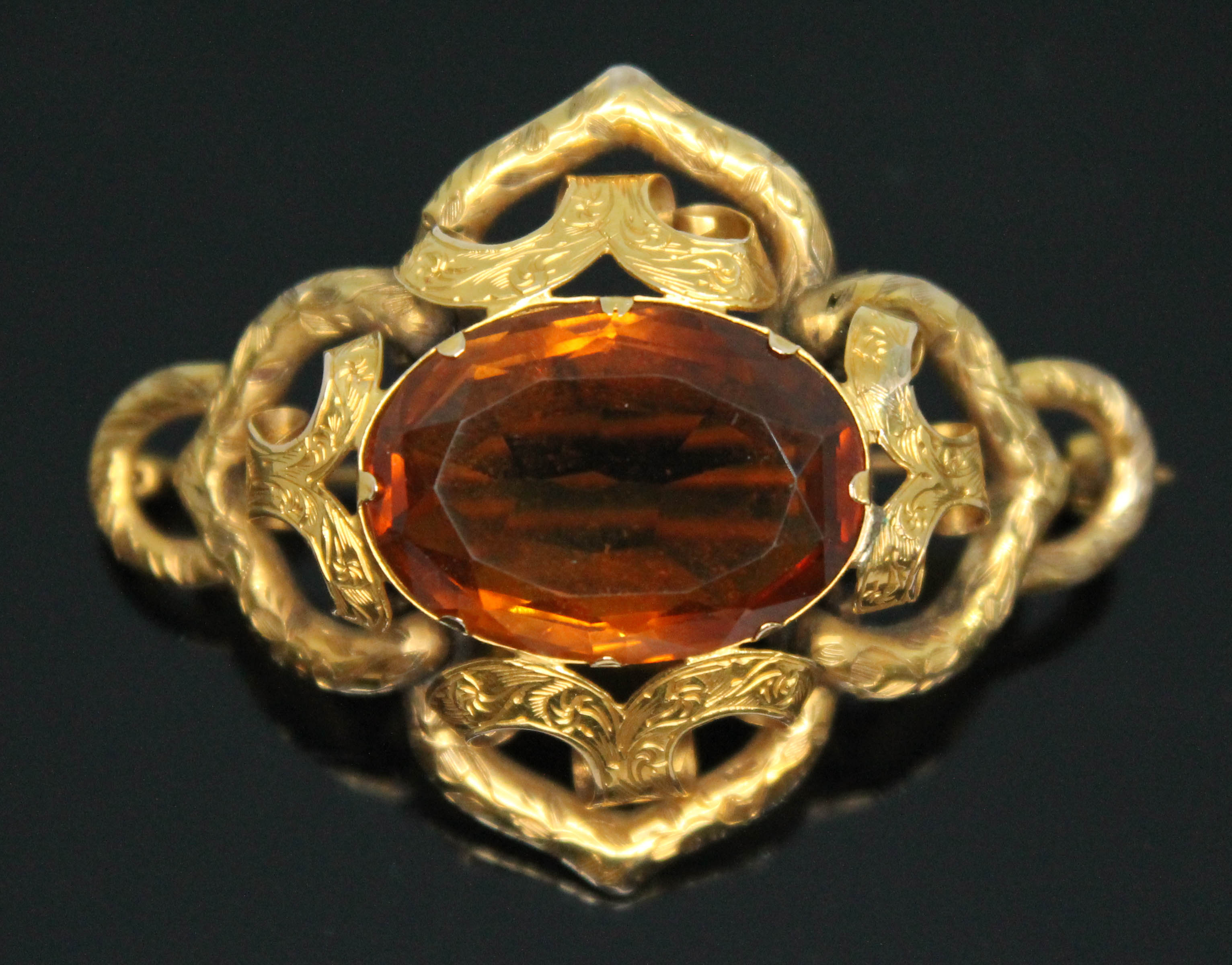 A Victorian yellow metal brooch of scroll form set with a central oval cut orange citrine weighing