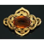 A Victorian yellow metal brooch of scroll form set with a central oval cut orange citrine weighing