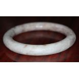 A Chinese jade bangle, carved cream and brown stone with scroll detail in relief to outer edge,