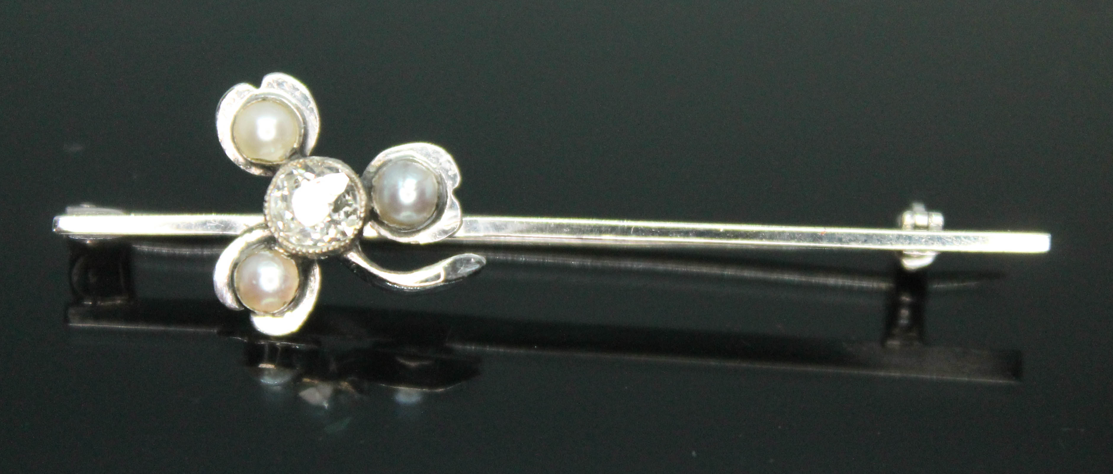 An Art Deco white metal bar brooch with applied shamrock set with three split pearls and a central