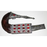 A Middle Eastern jambiya type dagger, white metal mounted eather scabbard set with red paste, length