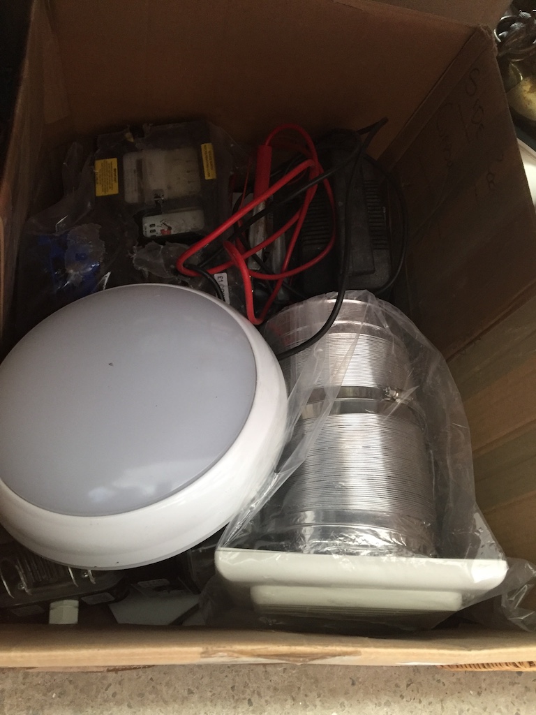 A box containing battery charger, pay as you go electric meter, expelair unit, 2 bulkhead lights,