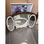 A wood framed oval mirror, a triple mirror, and a print of a clown playing a violin
