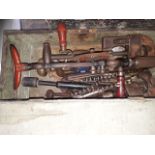 A wooden toolbox containing brace and bit drill, 2 stilsons and a mix of heavy tools