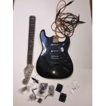 A black electric guitar in pieces. Stratocaster shape, pickguard has pots and pickups attached -