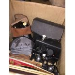 A box of assorted cameras and binoculars, also including a cigarette card album, Wheatons Atlas of