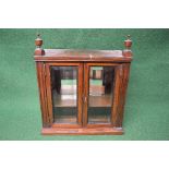 Rosewood wall cabinet having urn formed finials over two bevelled glazed doors opening to reveal