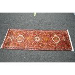 Small red ground carpet runner having blue, cream and mustard pattern with end tassels - 26.