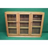 Blonde Ercol glazed bookcase having three doors each opening to reveal two adjustable shelves,