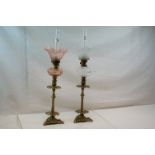 Two brass antique oil lamps with floral decoration, one with cranberry well and shade, the other
