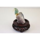 A small carved stone bird mounted on a crystal base on a wooden plinth.