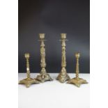 A pair of brass candlesticks mounted on square bases raised on floral feet together with another