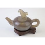 An oriental carved Jade teapot with bird decoration to lid on wooden stand.